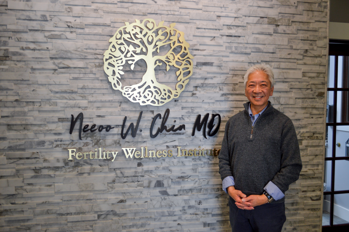 dr. chiun standing in front of a stone wall with the fertility wellness institute's logo